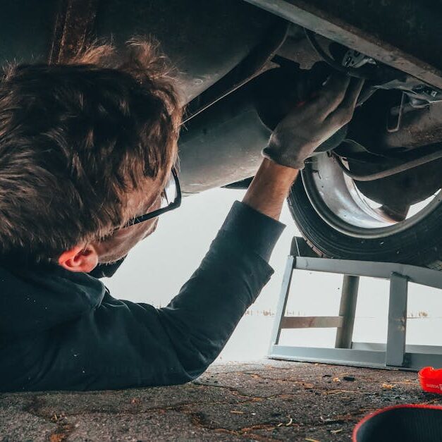 pexels-photo-2244746-2244746 Mechanic skillfully repairing car undercarriage in outdoor setting with tools.